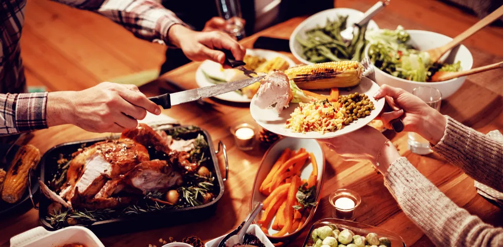 Hands serving a holiday meal with turkey, vegetables, and colorful side dishes on a festive dinner table.