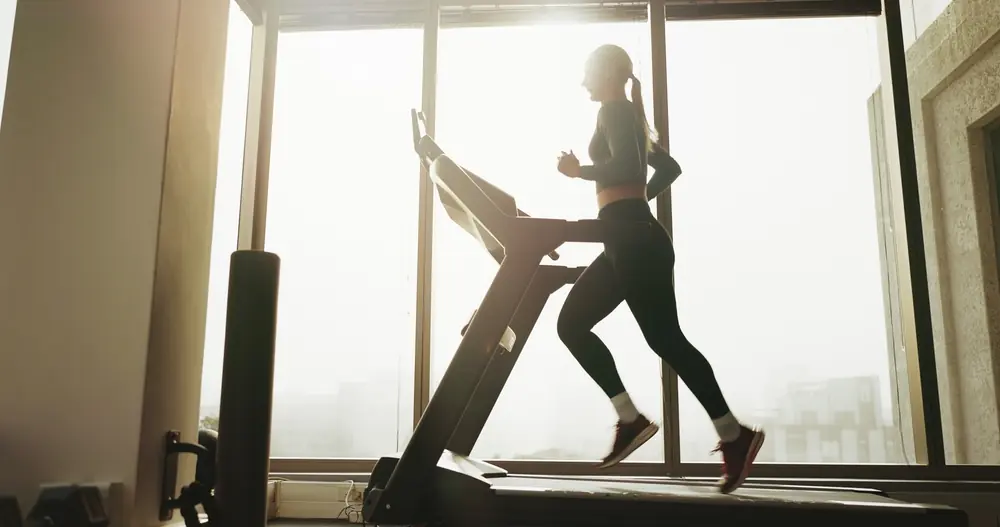 Woman walking on a treadmill at a steady pace, demonstrating Zone 2 cardio training for fat burning and metabolic health.